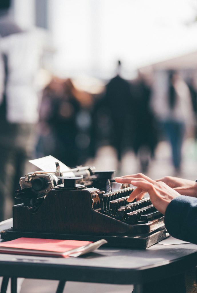 A writer sitting at a table typing on a typewriter.